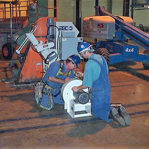 Two workers in hard hats and coveralls installing equipment